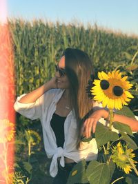 Woman wearing sunglasses while standing by sunflower plants against sky