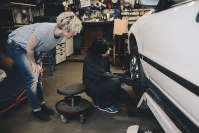 Customer looking at female mechanic examining car tire at auto repair shop