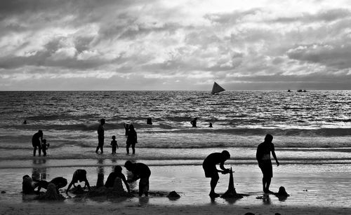 People enjoying at beach against cloudy sky