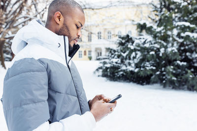 Young african man typing message, texting on phone, winter outdoor