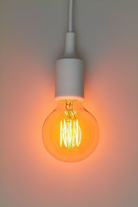 Close-up of illuminated electric bulb against wall