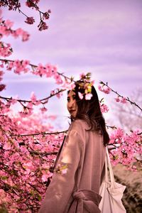 Low section of woman by cherry blossoms against sky