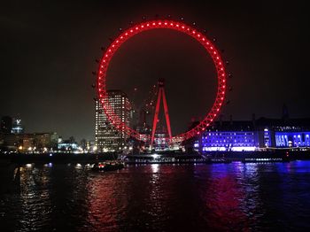 Illuminated ferris wheel by river at night