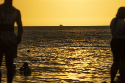 Silhouette people on beach against sky during sunset