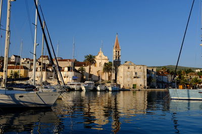 Sailboats moored at harbor by buildings against clear blue sky