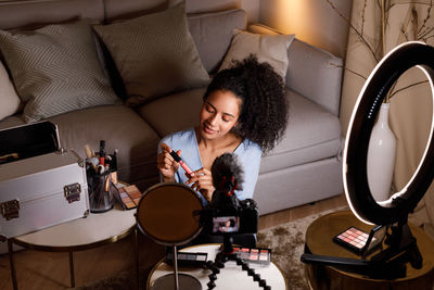 Camera filming young woman holding beauty product while sitting at home