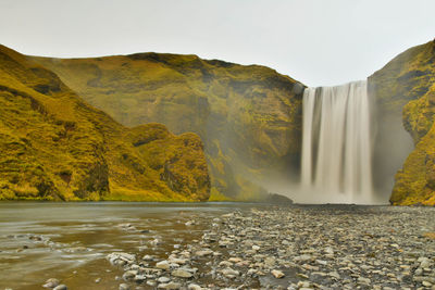 Scenic view of waterfall in mountains against sky