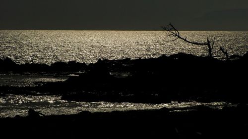 Silhouette landscape by sea against sky