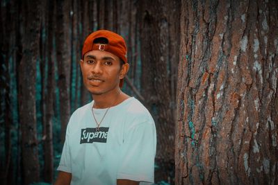 Portrait of young man standing against tree trunk