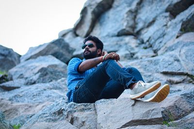 Young man looking away while sitting on rock