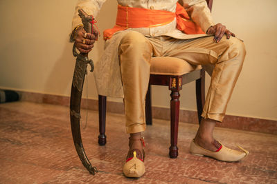 Low section of man wearing traditional clothing sitting on chair at home