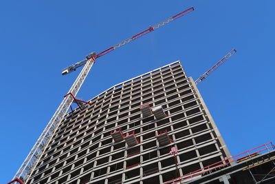 Low angle view of crane by building against clear blue sky