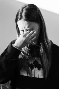 Girl touching eyes while standing against wall