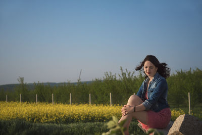 Woman sitting on field against clear sky