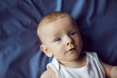 Baby boy blonde in white bodysuit lying on the bed