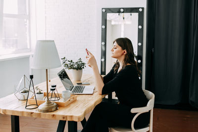 Side view of young woman sitting on table at home