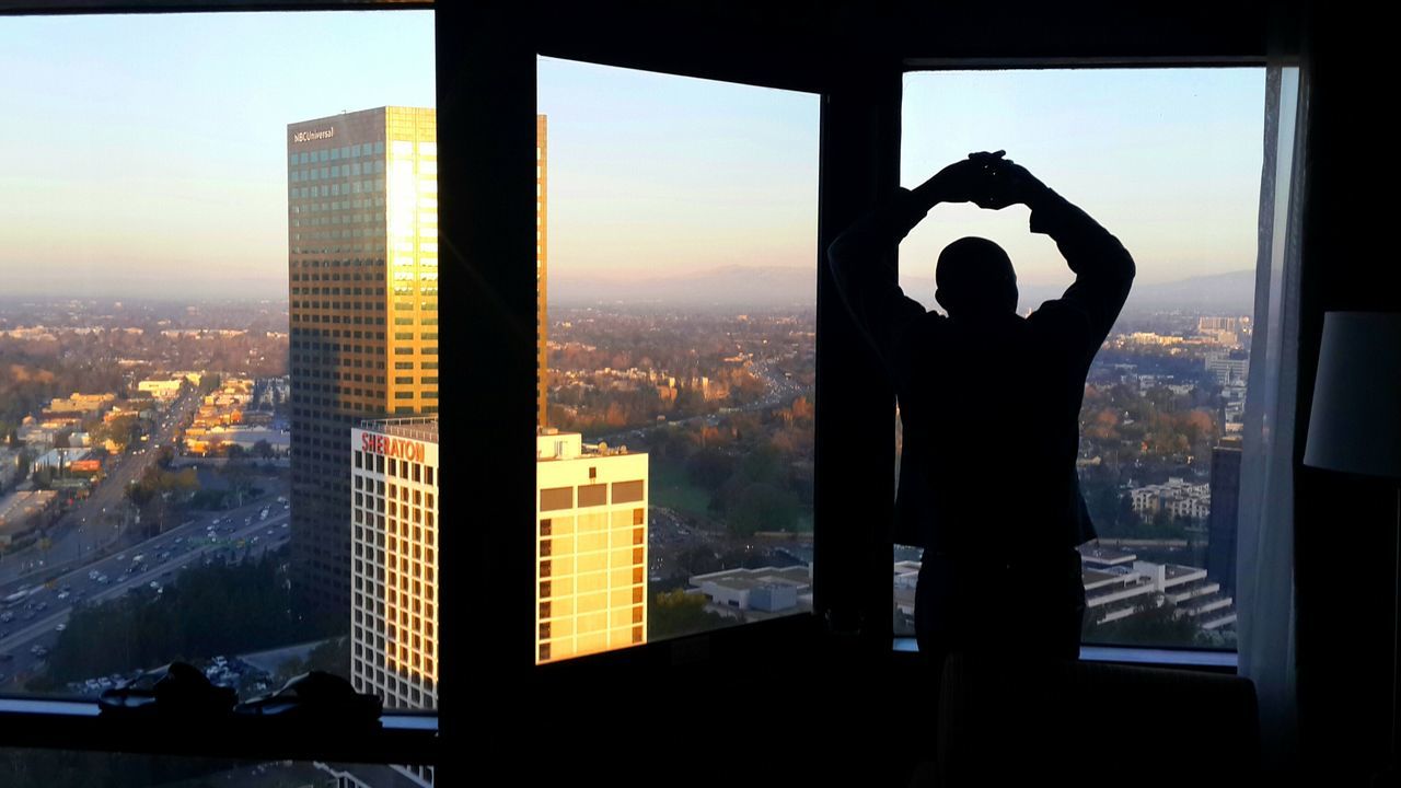 indoors, window, architecture, cityscape, built structure, glass - material, city, transparent, building exterior, silhouette, skyscraper, looking through window, sunset, sky, modern, sunlight, office building, residential building, home interior, residential structure