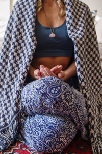 Woman wearing a crystal necklace meditation at home wrapped up in blanket