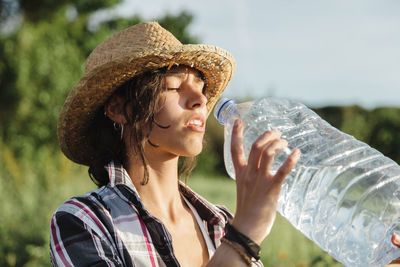 Woman wearing hat drinking water outdoors