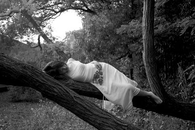 Woman relaxing on tree trunk in forest