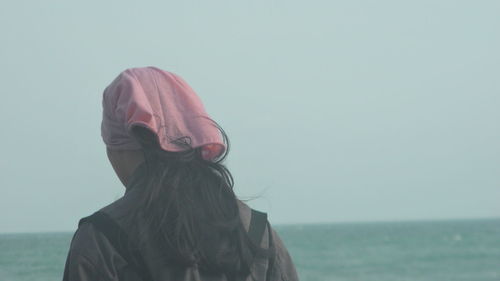 Rear view of young woman standing by sea against clear sky