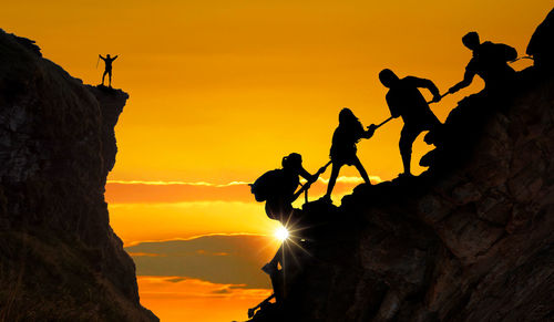 Silhouette people on rock against sky during sunset