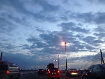 Cars moving on road against cloudy sky