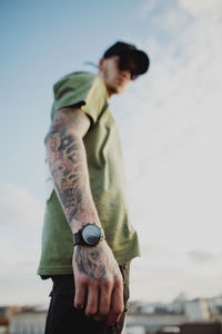 Young man looking away while standing against sky