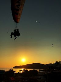 Silhouette people paragliding against sky during sunset