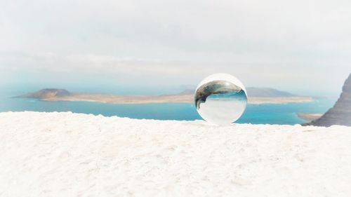 Close-up of crystal ball on beach against sky