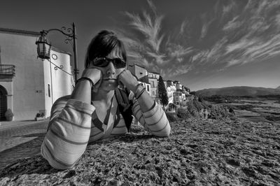 Upset woman with hand on chin leaning by houses in village against sky