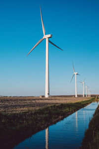 Windmills on field against clear blue sky