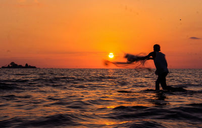 Silhouette man standing in sea against orange sky