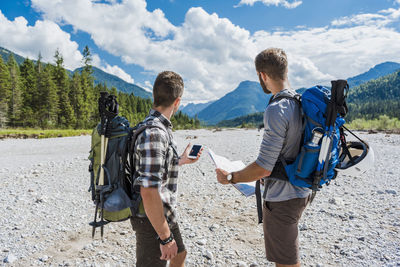 Germany, bavaria, two hikers standing in dry creek bed orientating with cell phone and map