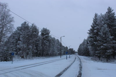 Snow covered road by trees against sky