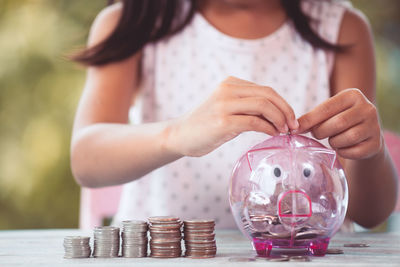 Midsection of girl putting coins in piggy bank on table