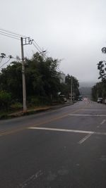 Empty road by trees against sky