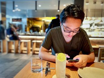 Young asian man using mobile phone at table inside restaurant.