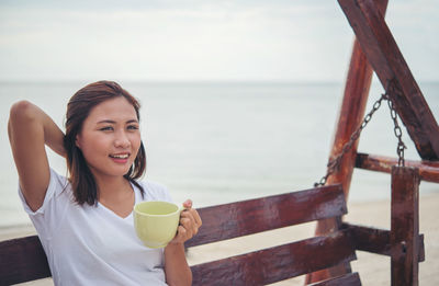 Portrait of woman having coffee on bench at beach