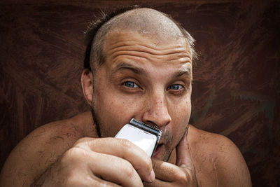 Close-up portrait of shirtless man holding smart phone