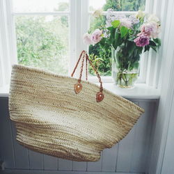 Close-up of straw bag by vase on window at home