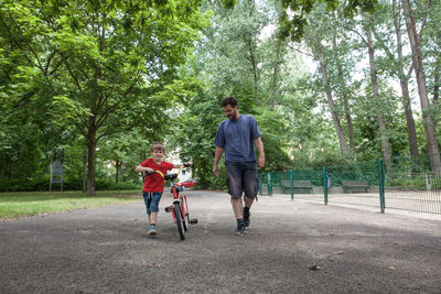 Full length of father and son with bicycle walking in park