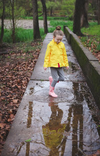 Full length of girl jumping in puddle during rainy season