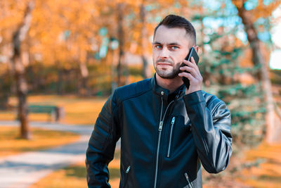 Young man using mobile phone while standing outdoors during autumn
