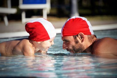 Side view of playful father and daughter swimming in pool