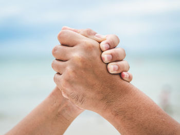 Close-up of man holding hands against sea