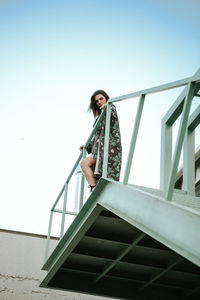 Low angle view of woman standing on staircase against sky