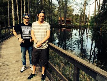 Portrait of friends standing on footbridge over lake