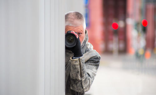 Portrait of man photographing with digital camera by wall