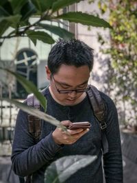 Young man using mobile phone outdoors against ivy covered wall and reflective windows.